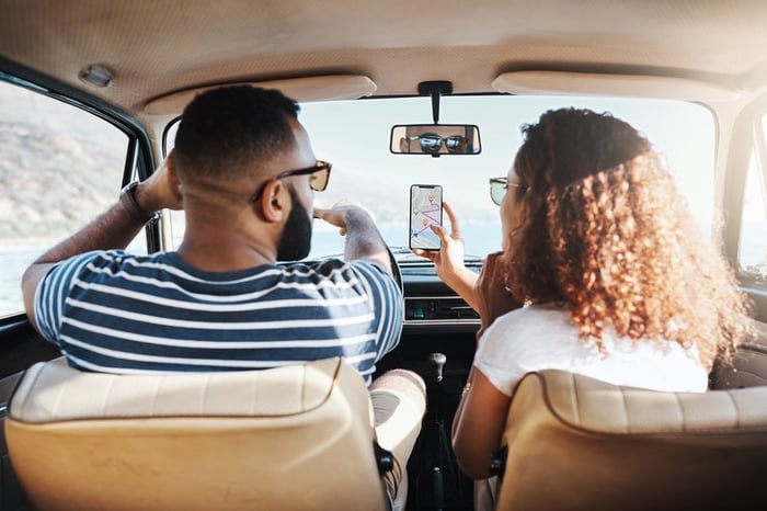 Two people driving in a car on a sunny day while looking up directions on a smartphone.