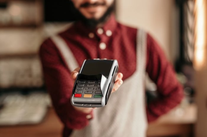 A waiter wearing an apron and holding up a credit card reader awaiting payment.