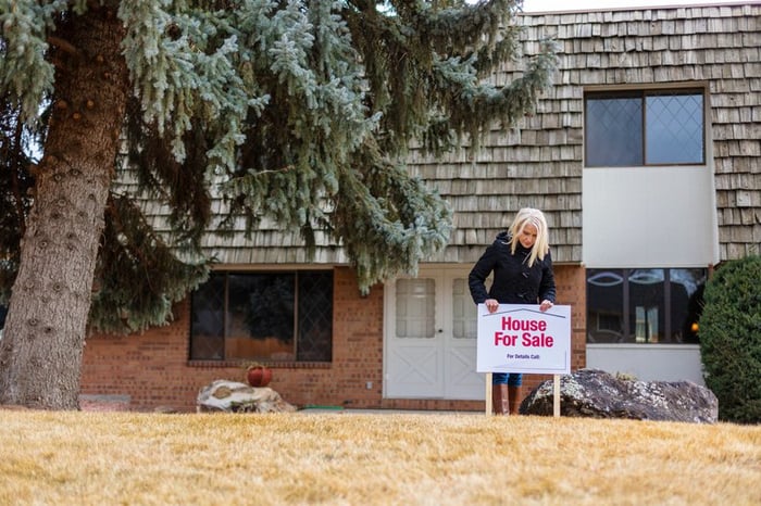 A person putting a House for Sale sign in the front lawn of their property.