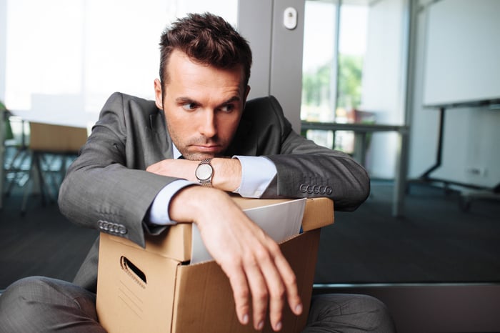Person wearing suit looks dejected while holding box