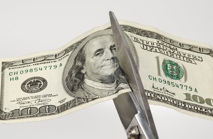Scissors cutting a one-hundred-dollar bill in half. 