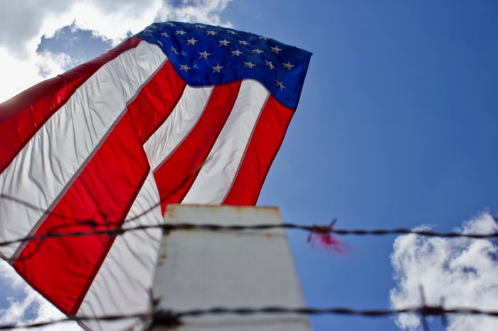 A large American flag hanging behind a barbed-wire fence. 